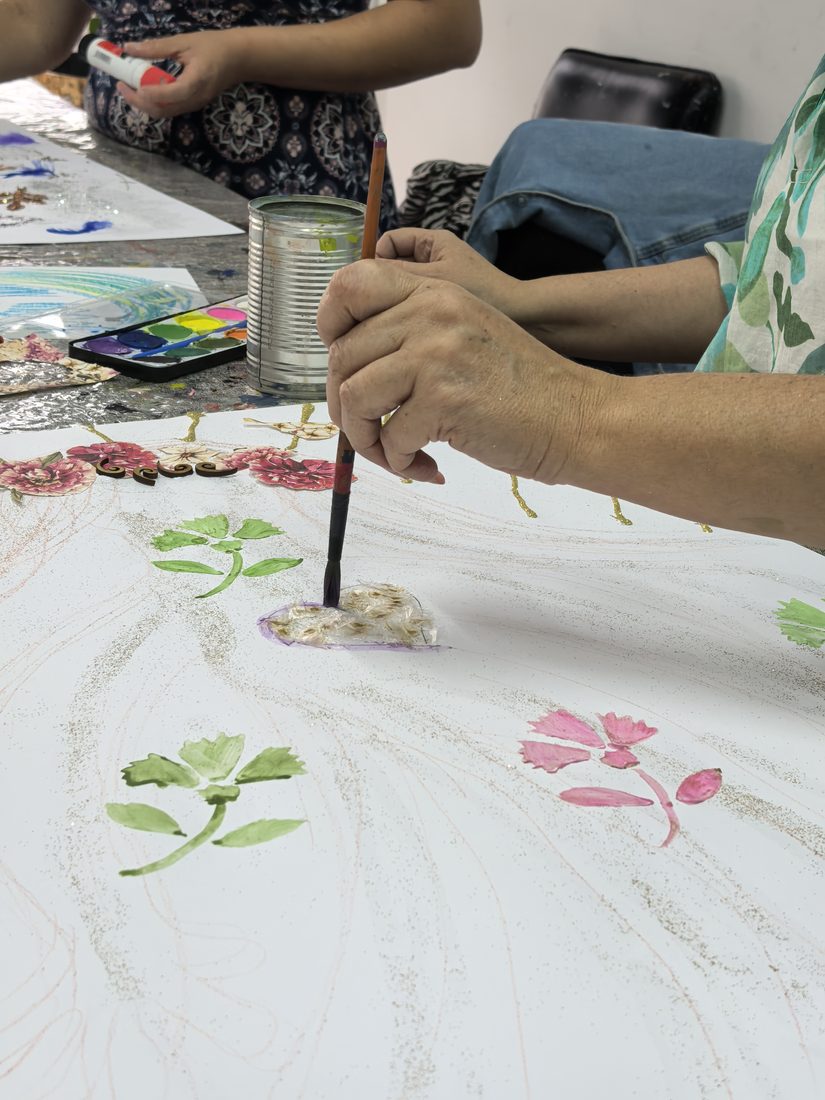 Manos pintando flores con acuarela sobre papel durante un taller